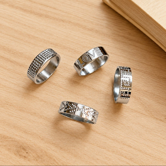 Four silver rings with intricate designs on a light surface.